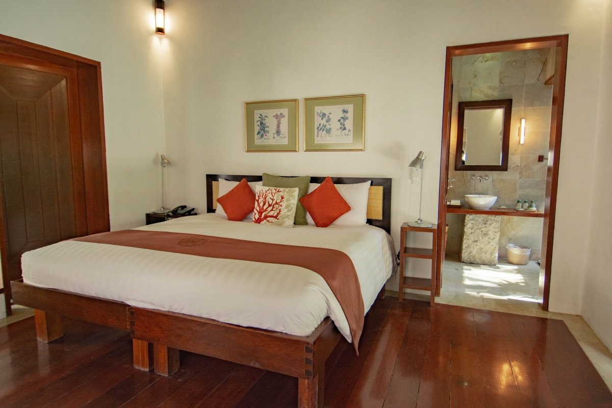 Hotel room featuring a large bed with white linens, decorative pillows, and a wooden headboard, with an adjacent bathroom visible through an open doorway.