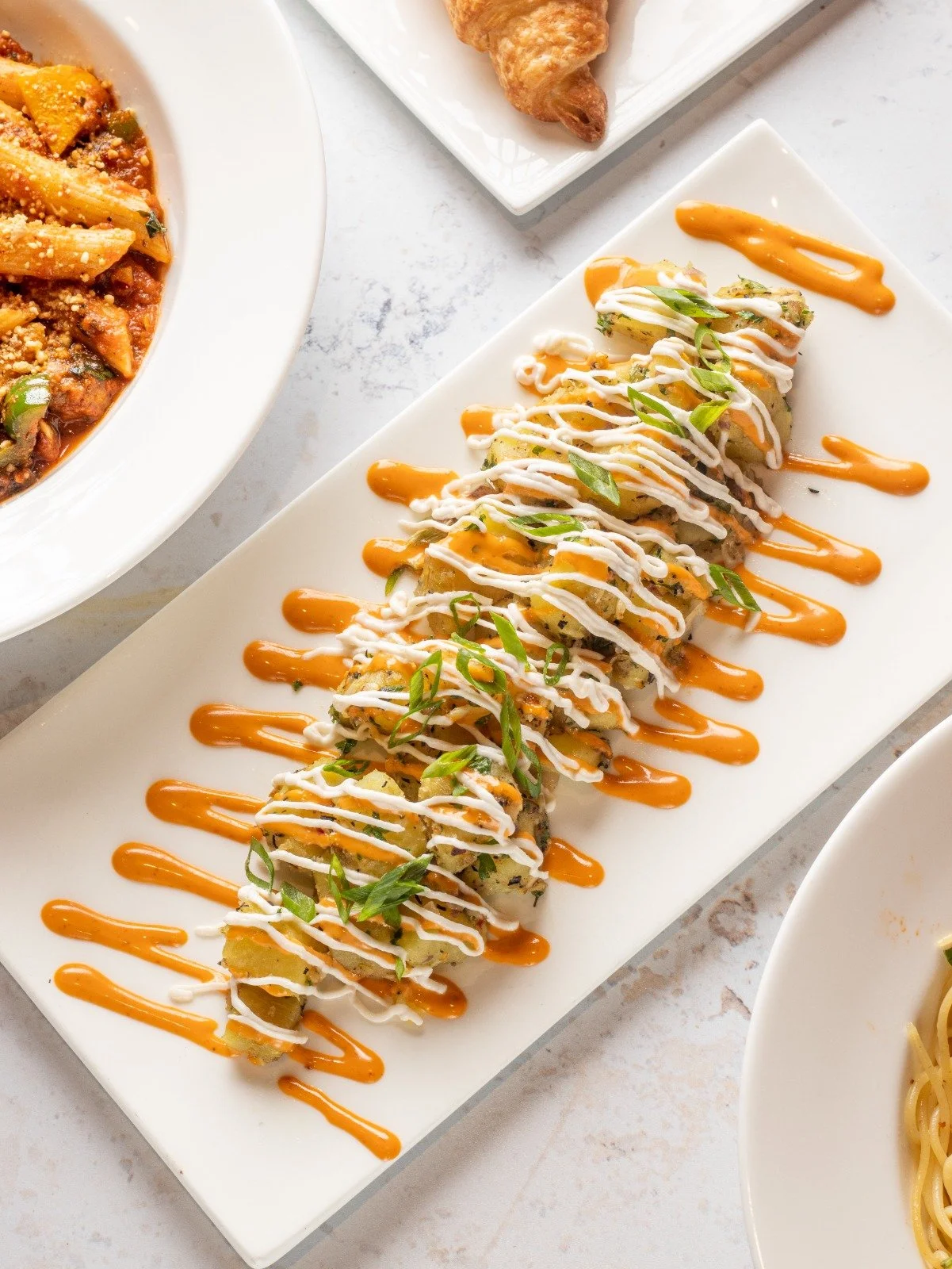 A plate of sushi rolls topped with white and orange sauces, garnished with sliced green onions.