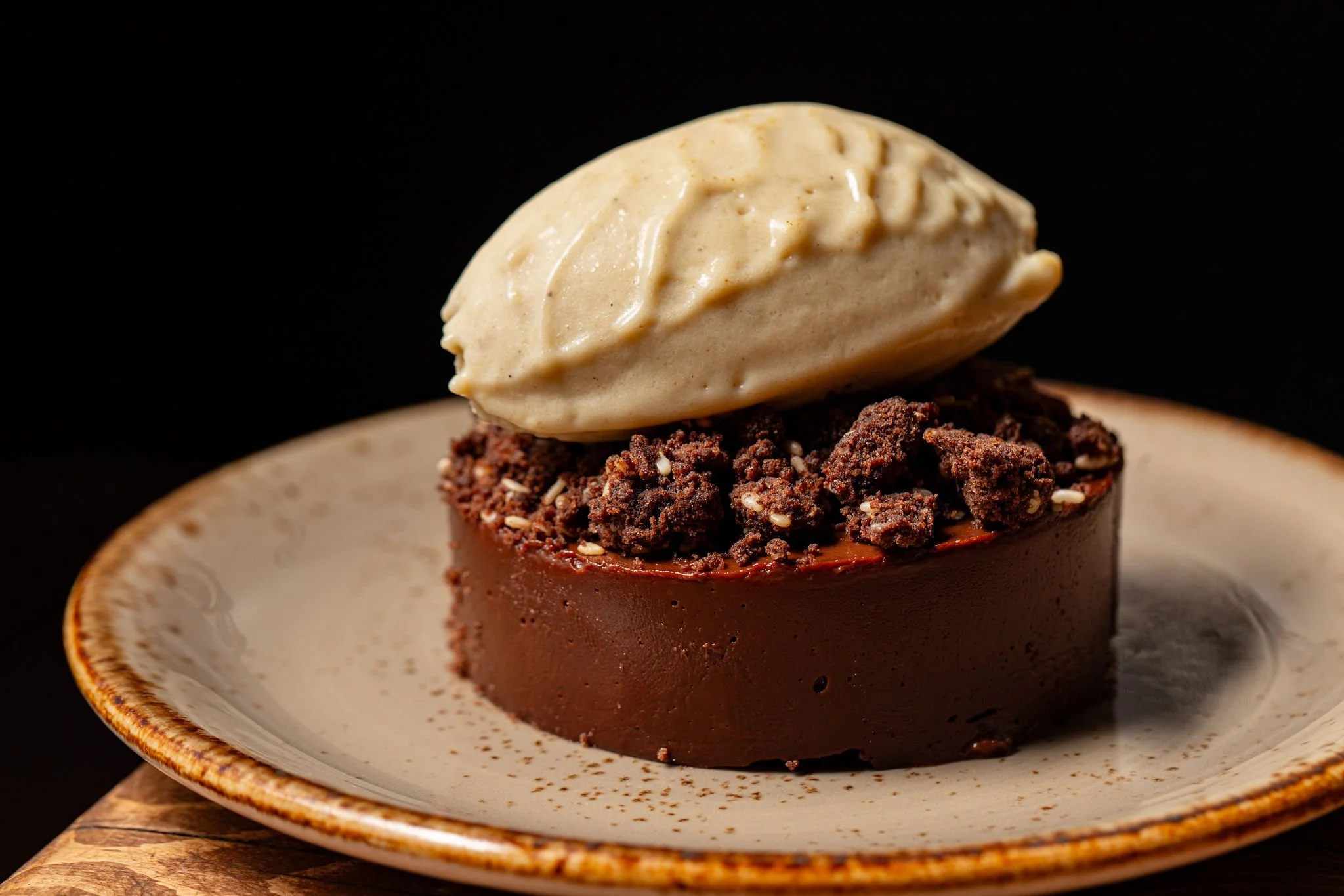A chocolate cup filled with crumbled cookie topping and topped with a dollop of vanilla ice cream, served on a ceramic plate.