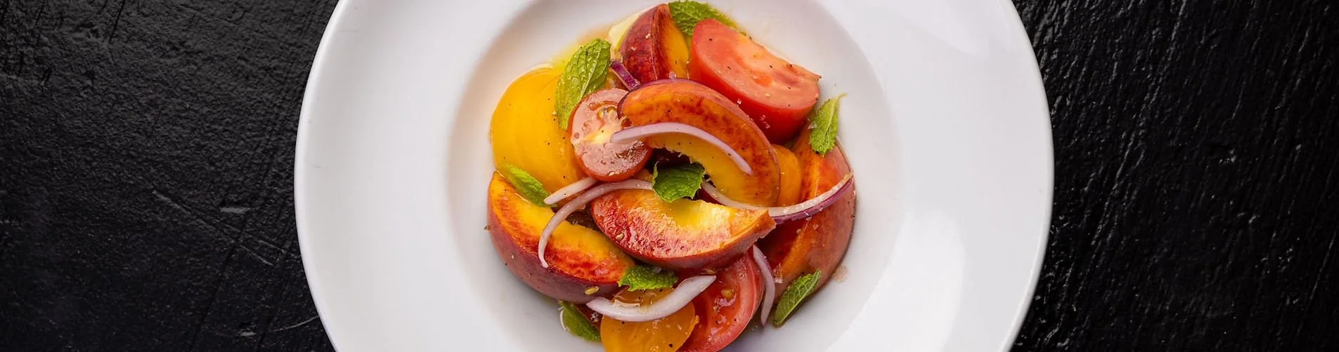 A plate of fresh tomato salad with slices of red, yellow, and orange tomatoes, garnished with green herbs and thin onion slices.