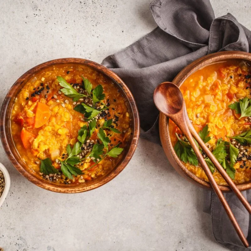 Two bowls of vegetable curry garnished with parsley and sesame seeds, with a gray cloth napkin nearby.