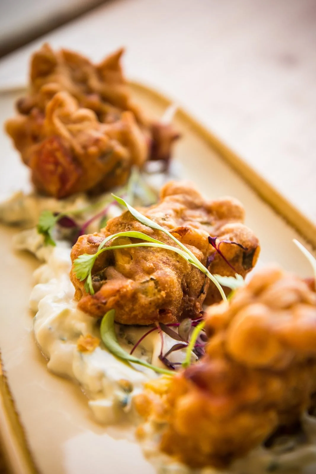 Close-up of Indian or Pakistani-style fried chicken pieces garnished with microgreens on a bed of creamy sauce, served on a white platter.