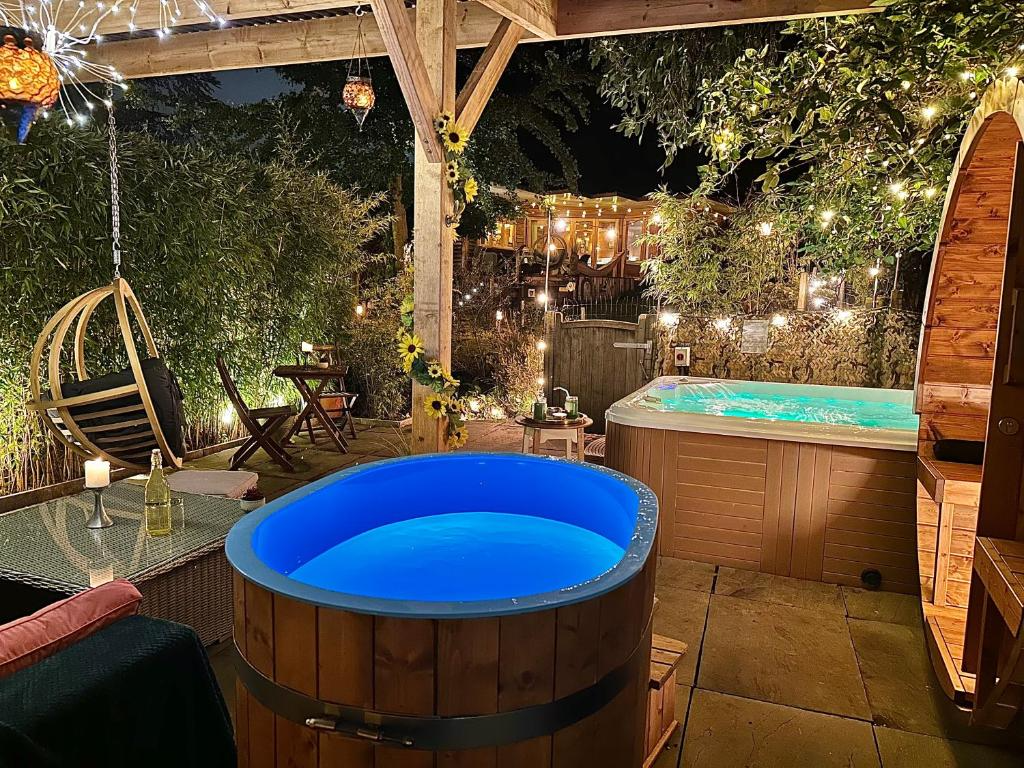 Nighttime outdoor patio with two hot tubs, wooden furniture, hanging swing chair, string lights, candles, and lush greenery.