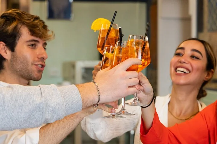 People clinking glasses of orange-colored drinks with lemon slices for a toast at a social gathering.