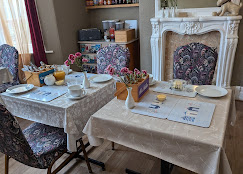A dining table set with plates, cups, and utensils in a room with a fireplace and patterned chairs.