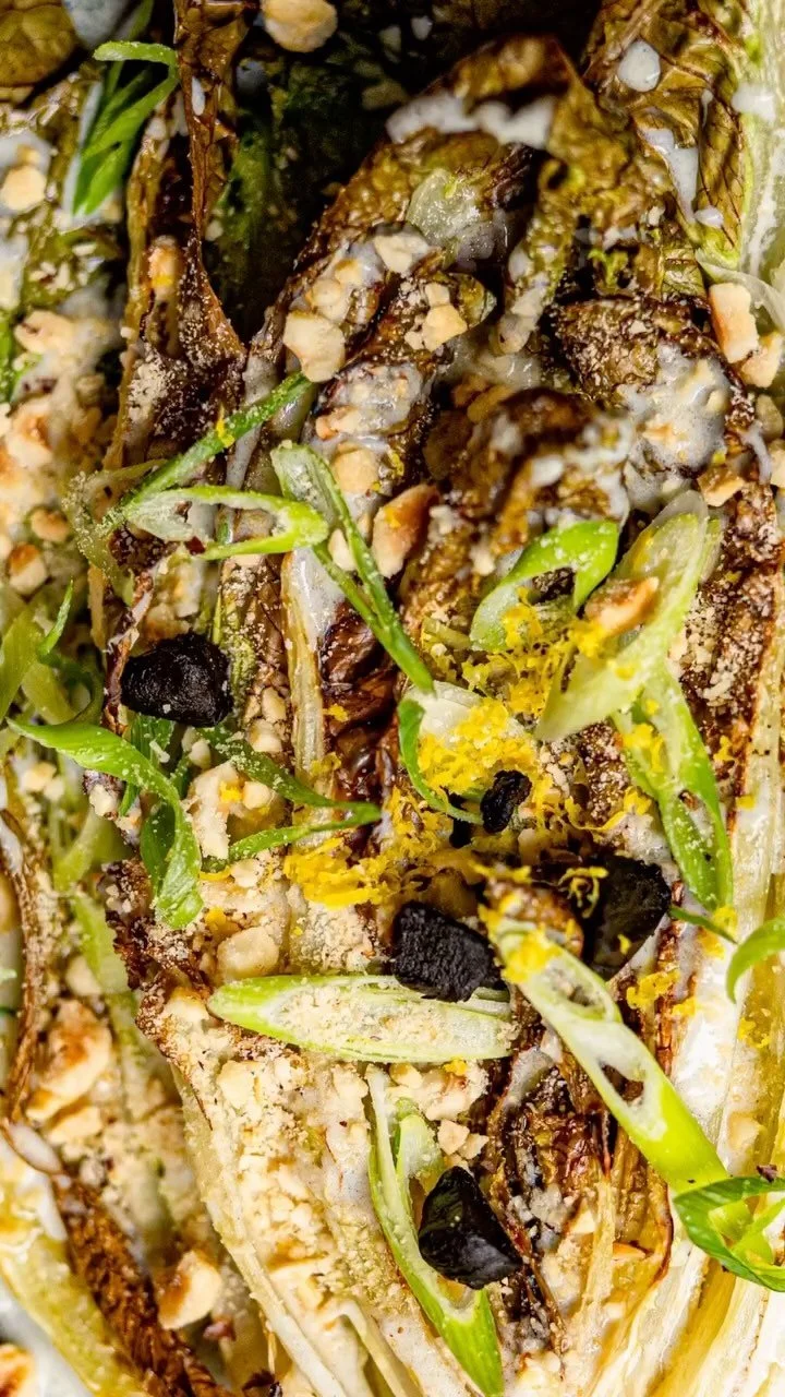 Close-up of roasted or grilled fish garnished with green herbs, crushed nuts, black pepper, egg yolk, and possibly some seasoning or sauce.