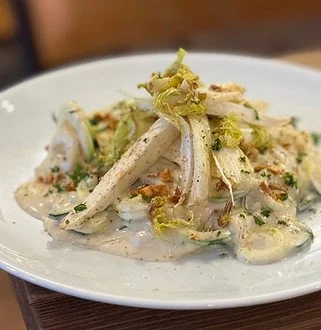 A white plate with chicken and vegetables in a creamy sauce, garnished with lettuce.