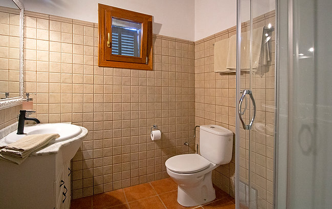 Bathroom with beige tiled walls, small window, white toilet, sink with towel, and a shower stall with glass door.