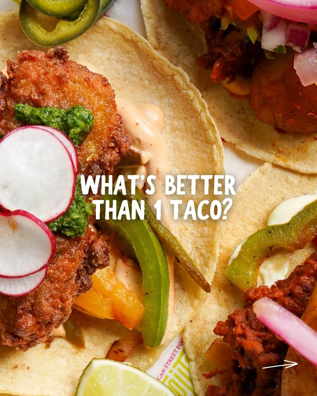 Close-up of two tacos filled with fried chicken, vegetables, radishes, and sauces, with lime wedge, jalapeños, and onion in background, with the text 'What's better than 1 taco?'