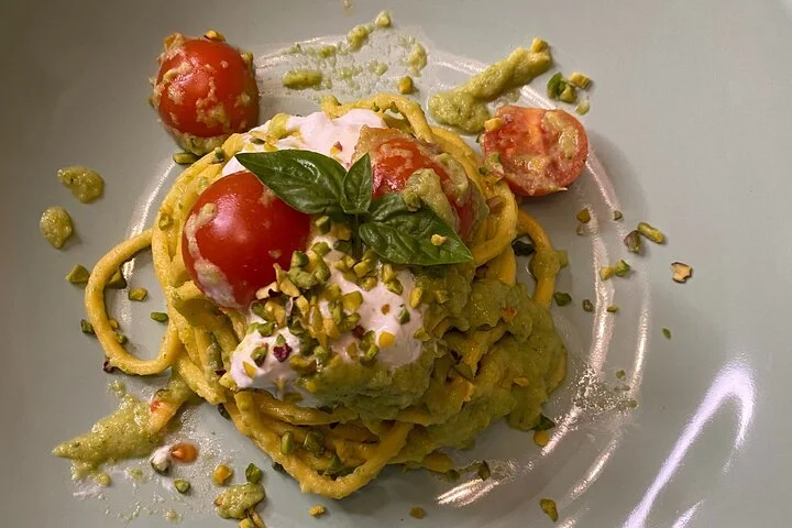 A plate of pasta topped with cherry tomatoes, basil leaves, and pesto sauce.
