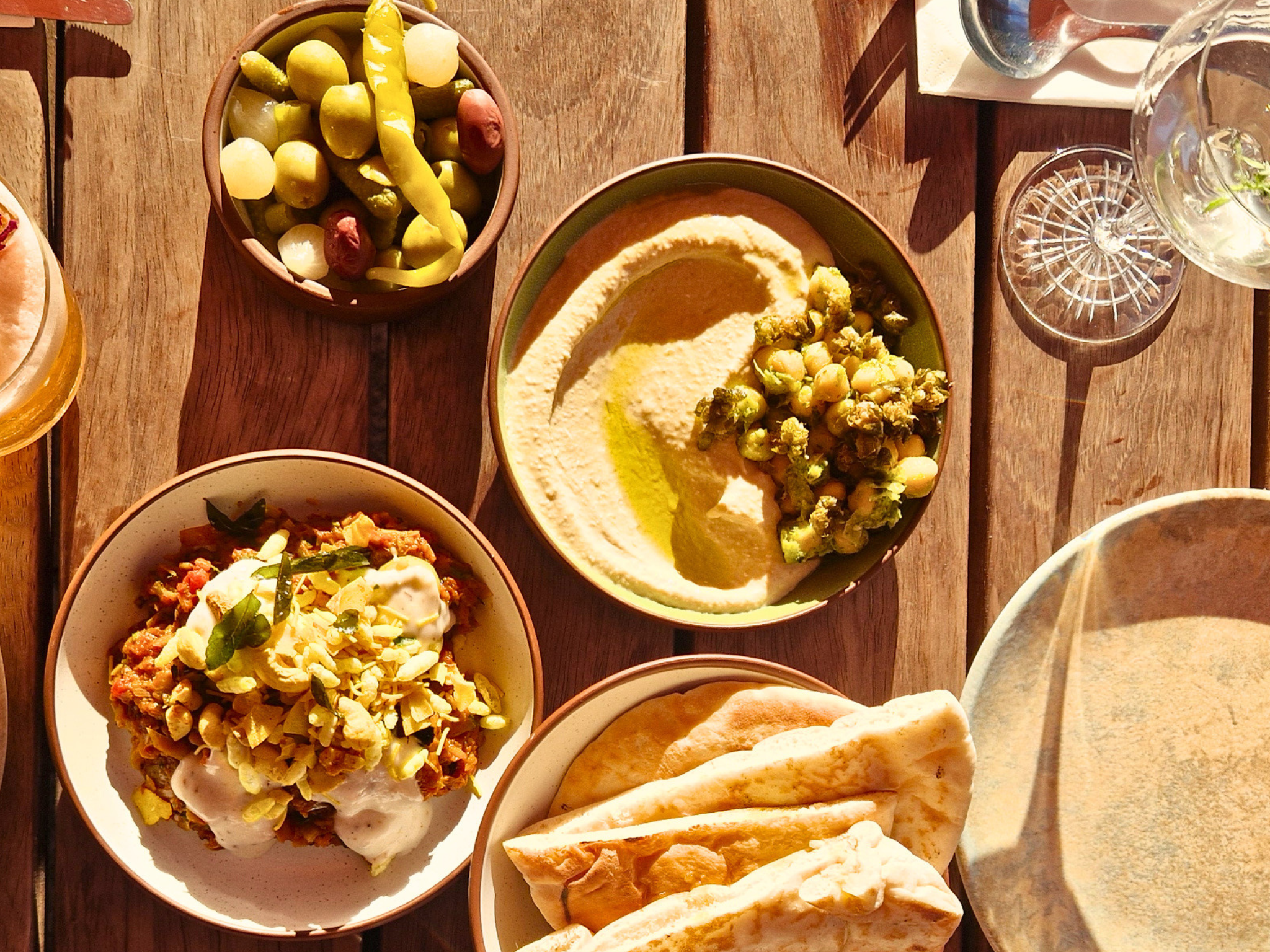 Assorted dishes of hummus, pickles, and salads on a wooden table.