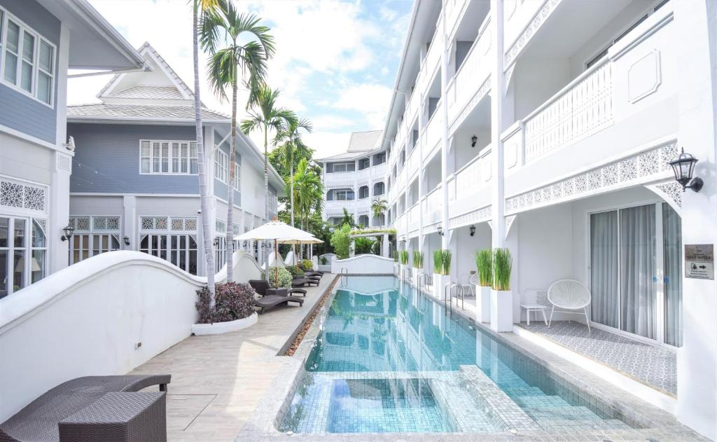 Outdoor hotel pool area with lounge chairs, umbrellas, palm trees, and white building facades in a tropical setting