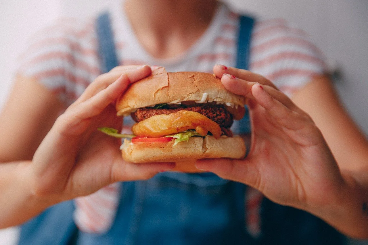A person holding a hamburger with lettuce, tomato, cheese, and a beef patty