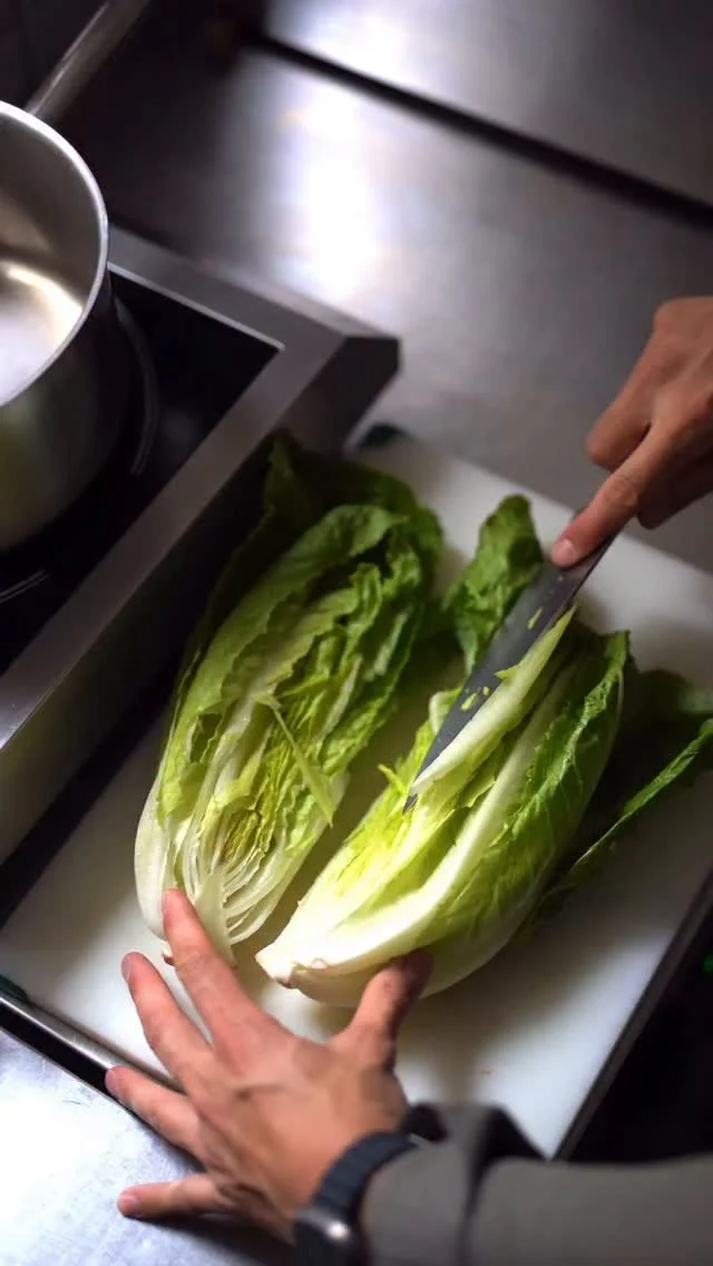Person slicing a head of romaine lettuce on a cutting board in a kitchen.