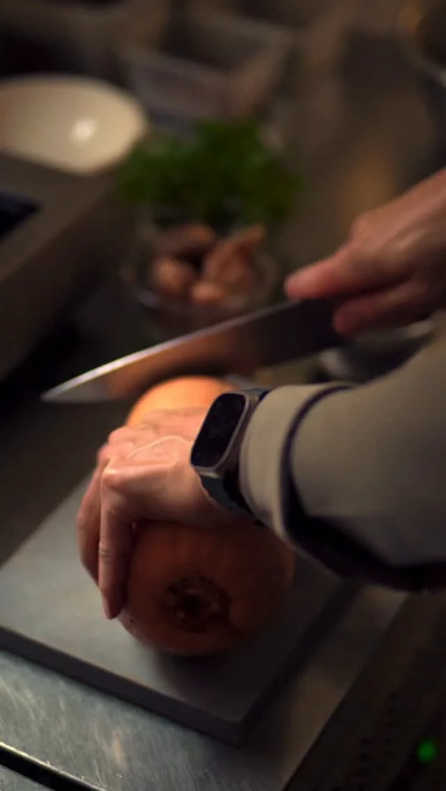 Person slicing a cake or bread with a knife in a kitchen with a plant and other items in the background.