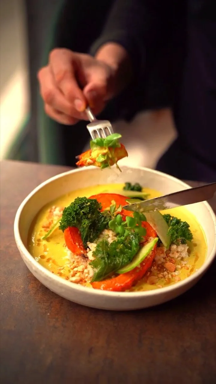 A person holding a fork with a bite of colorful vegetable soup with broccoli, tomato, and greens in a bowl.
