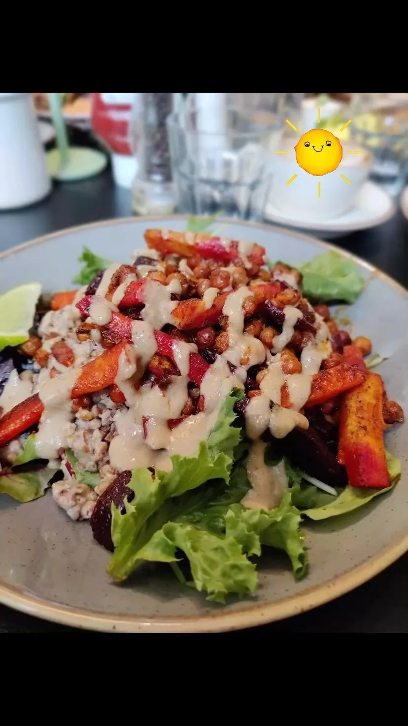 Salad with lettuce, roasted vegetables, beans, and creamy dressing on a plate, with a lemon wedge on the side, on a table with glasses and condiments in the background.