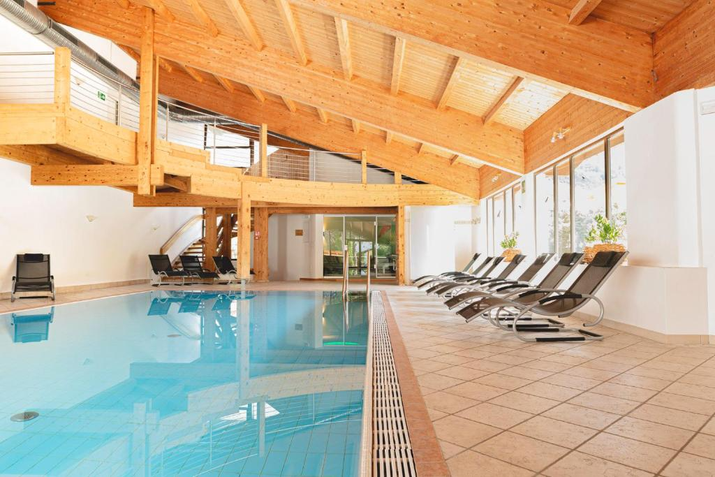 Indoor swimming pool area with lounge chairs, large windows, and wooden ceiling.