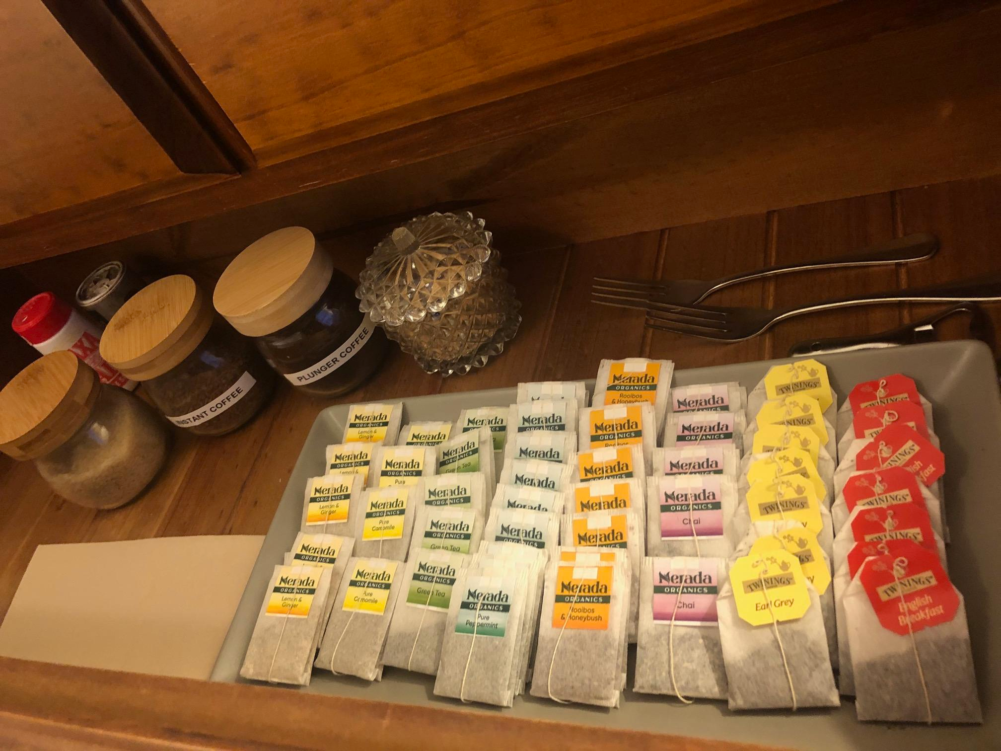 Assorted tea bags on a tray, with containers of coffee labeled 'Plant Coffee' and a glass ornament on a wooden surface.