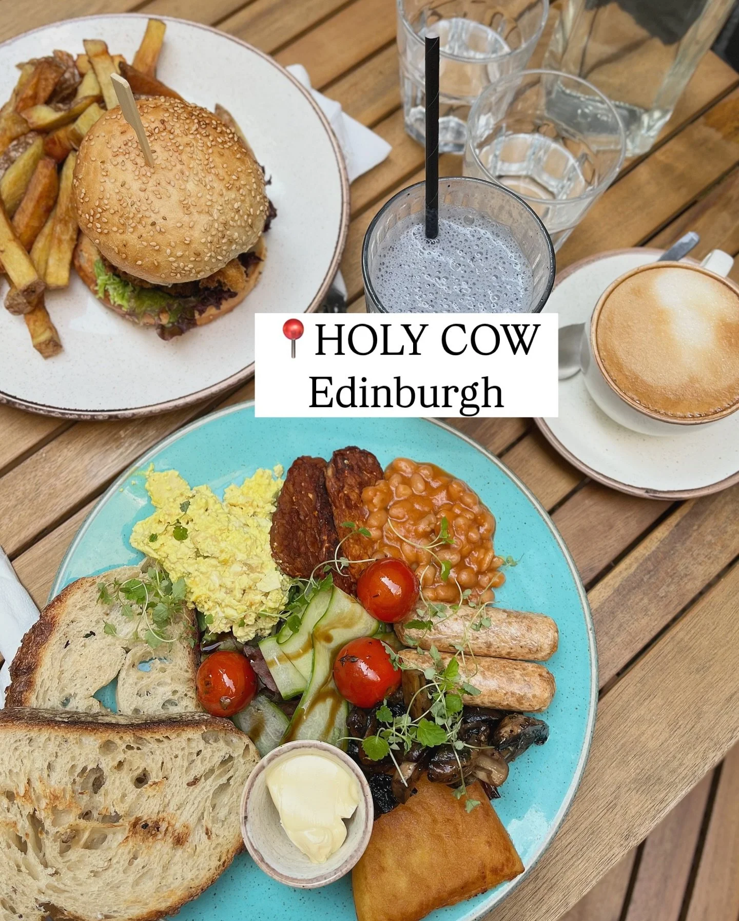 A plate of mixed Scottish breakfast items including smoked salmon, toast, cherry tomatoes, sautéed mushrooms, and scrambled eggs, served on a blue plate. Also visible are glasses of water and a cup of coffee on a wooden table.