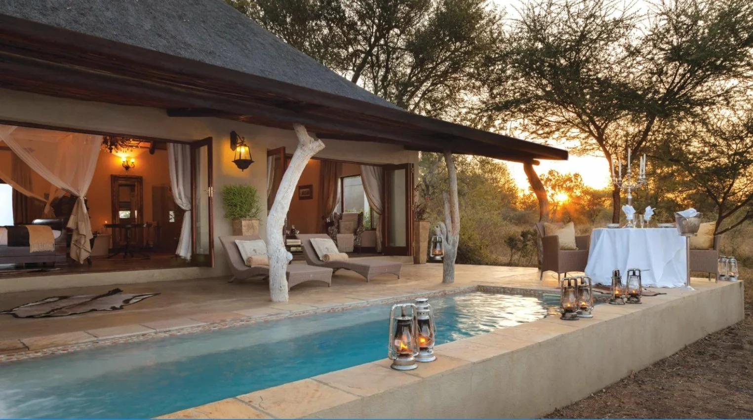 Luxury outdoor pool area at sunset with tables, chairs, and candles, overlooking a natural landscape.