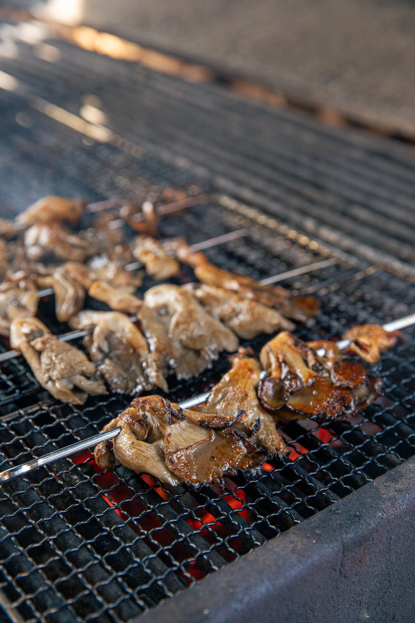 Meat grilling on a barbecue with a metal grate over red-hot charcoal.