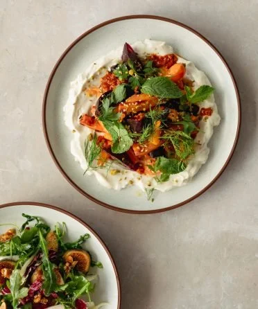 Two bowls of salad, one with mixed greens, cherry tomatoes, herbs, and possibly grilled vegetables, and the other with mixed greens and toasted nuts.