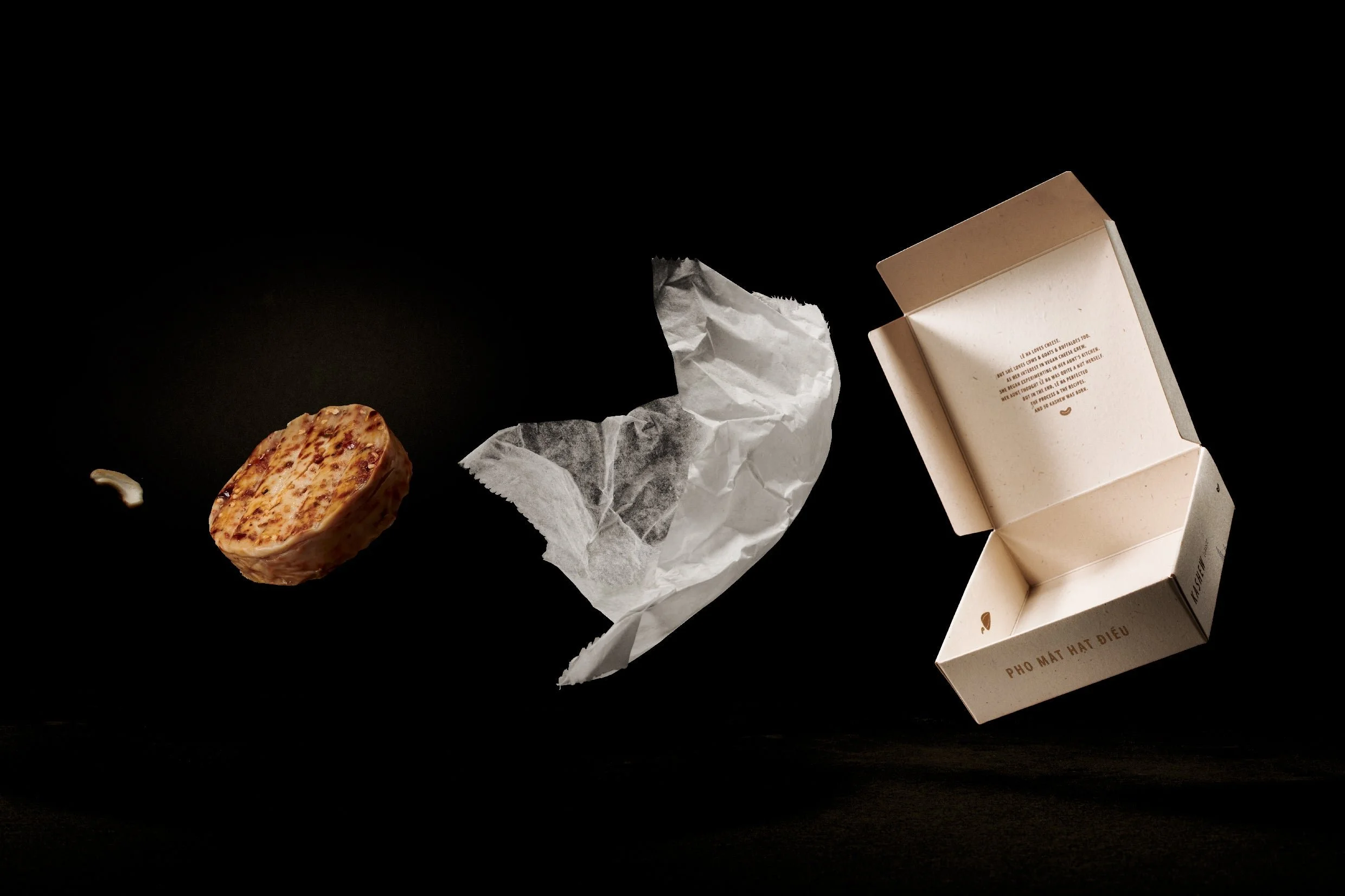 A partially opened takeout box, crumpled paper, and a food item on a black surface.