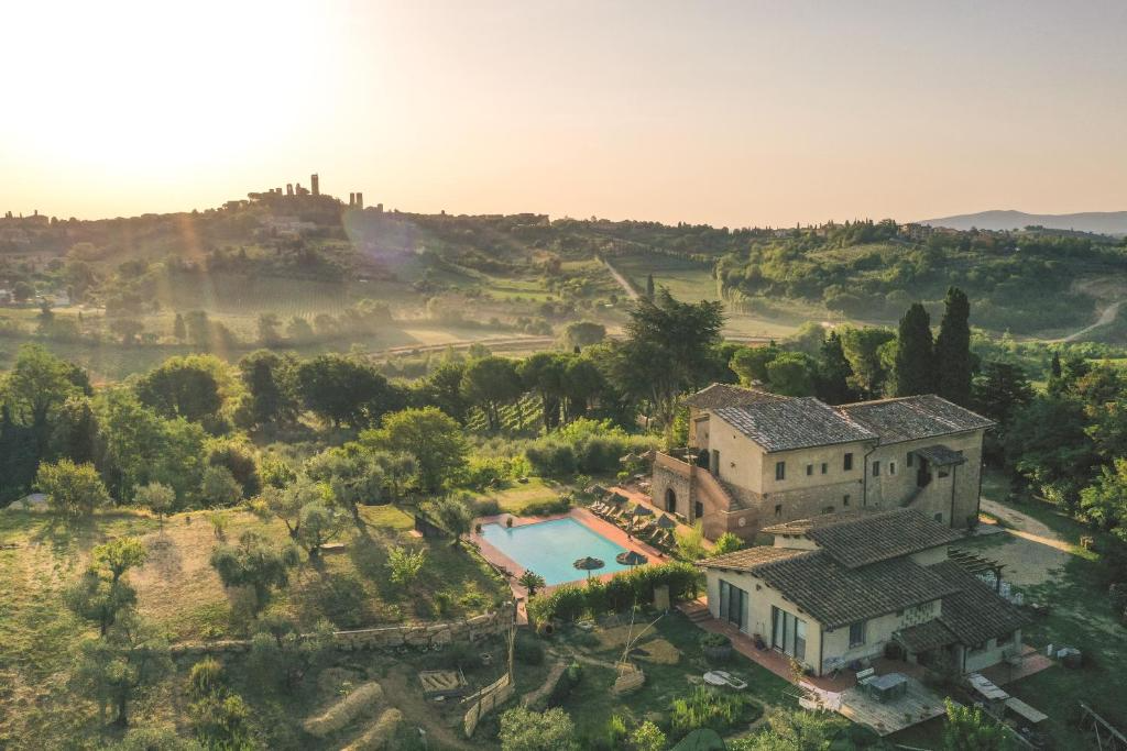 Aerial view of a countryside home with a swimming pool, surrounded by trees and rolling hills during sunset.