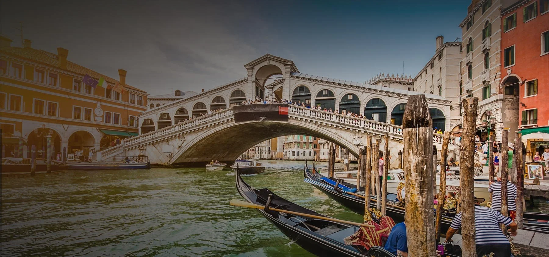Venetian gondolas docked on a canal with the Rialto Bridge and historic buildings in Venice, Italy