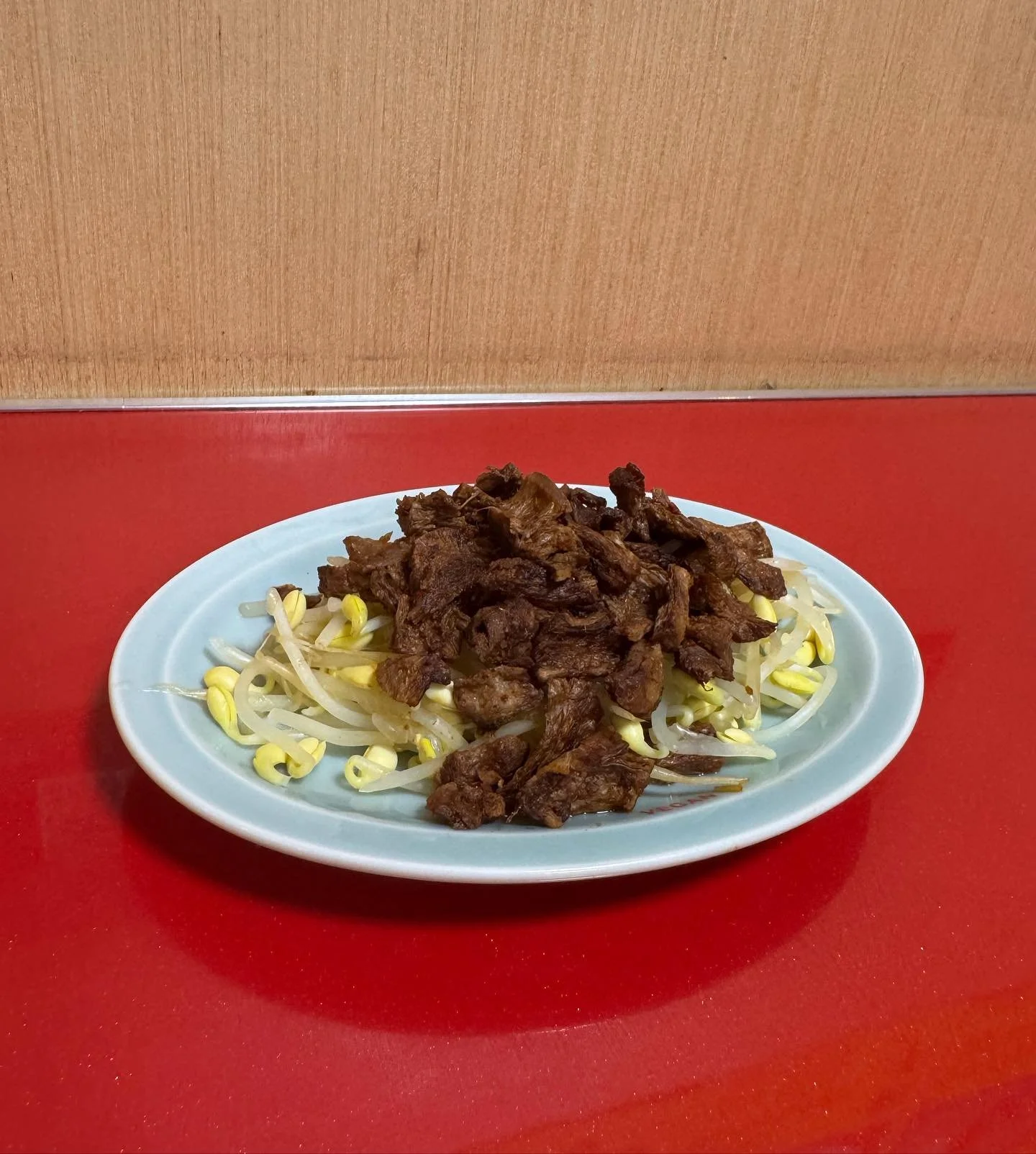 A white oval plate with stir-fried beef and bean sprouts on a red table.