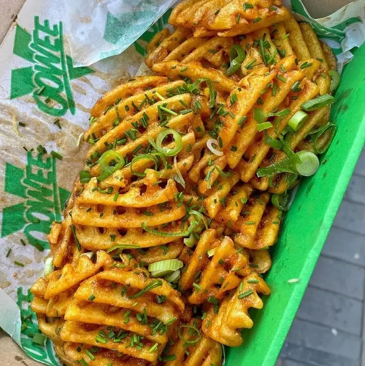 Fried waffle-cut fries topped with chopped green onions and herbs in a green basket lined with Guy Fieri's food truck paper.