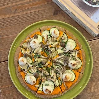 Vegetable pizza topped with zucchini, mushrooms, and cheese on a green plate.