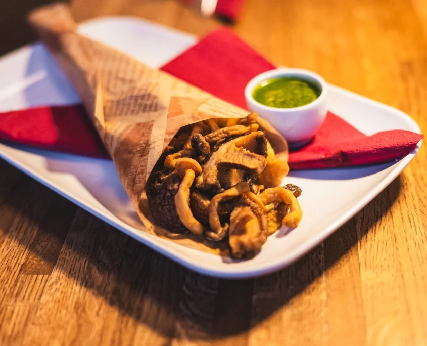 Fried calamari with a side of green dipping sauce on a white plate with a red napkin, placed on a wooden table.