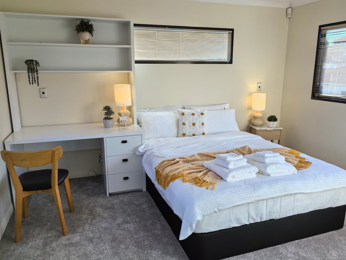 A bedroom with a bed, nightstands, lamps, a desk, and shelves.