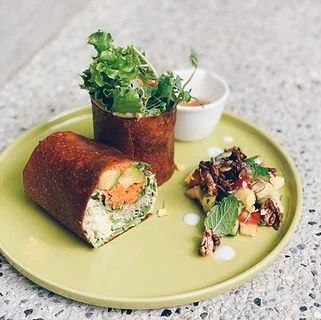 A green plate holding a sushi roll, a small bowl of dipping sauce, and a salad with greens, nuts, and dressing, with a speckled countertop background.