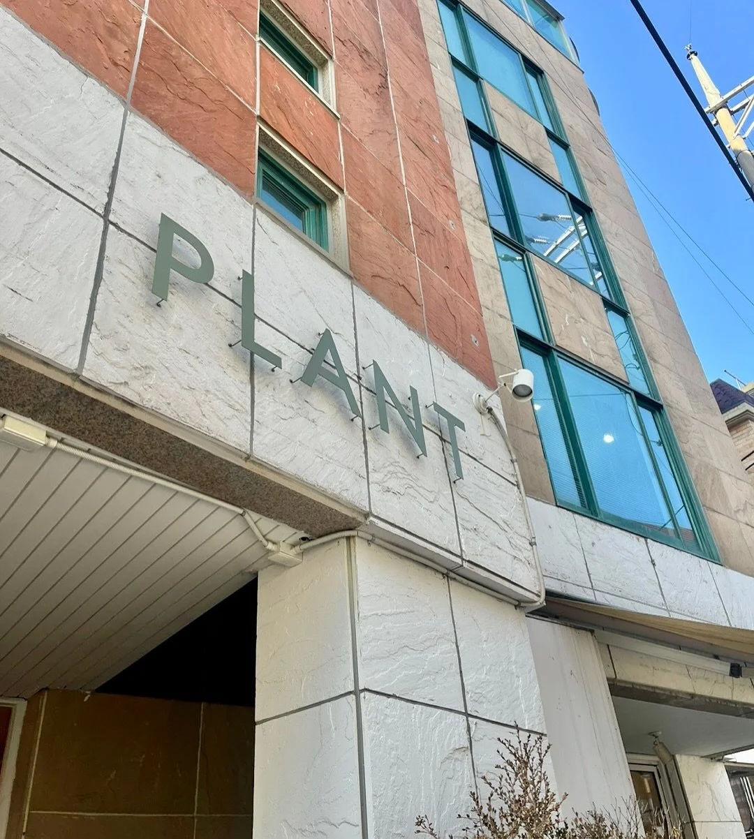 Exterior view of a modern building with the word 'PLANT' on a sign above the entrance.