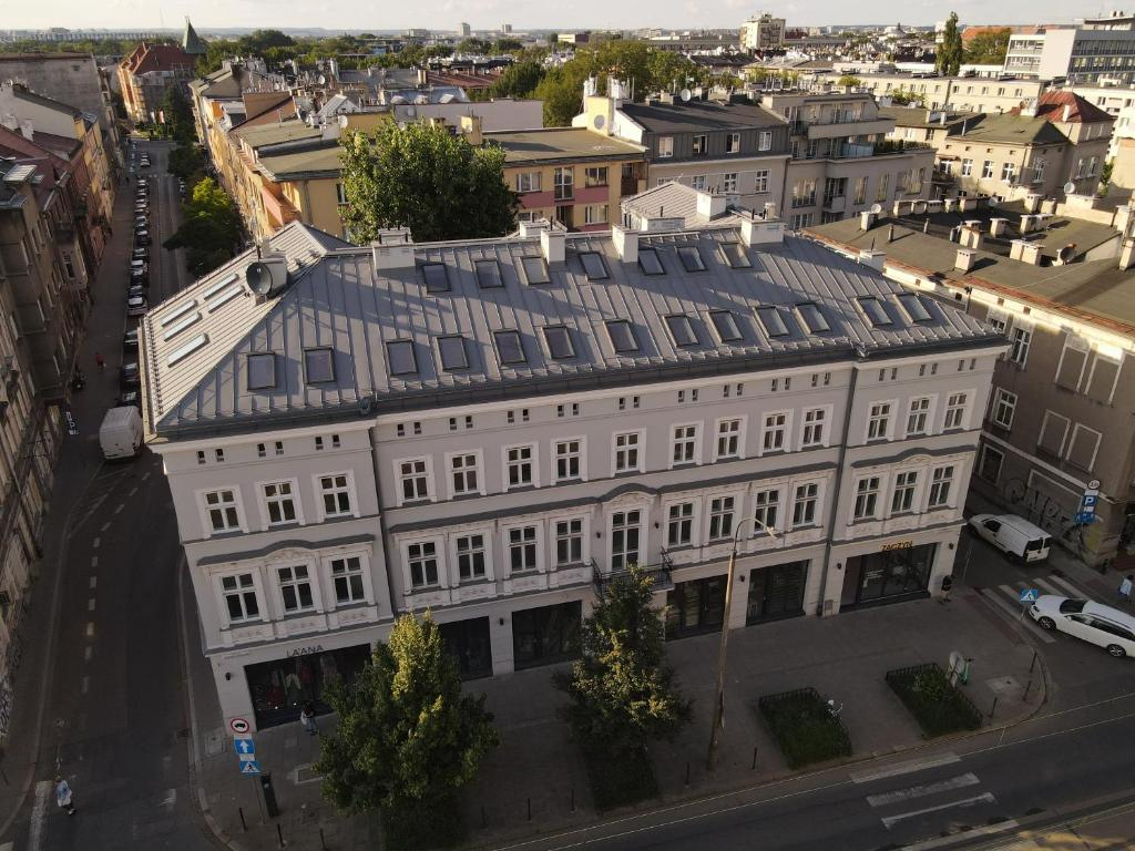 A multi-story white building with a gray metal roof, situated on a city street corner, surrounded by other buildings and trees.