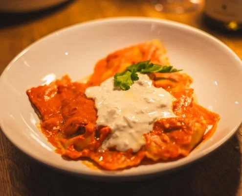 A bowl of lasagna with melted cheese, topped with a dollop of sour cream or white sauce, garnished with a sprig of cilantro