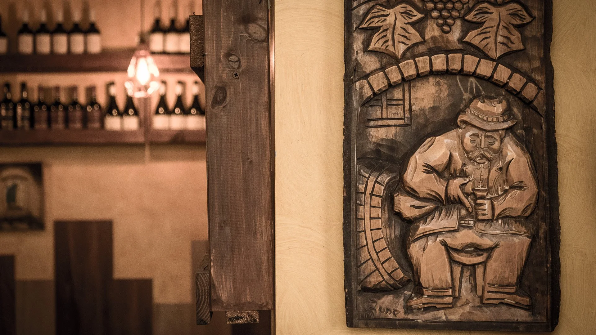 Wooden carved art piece depicting a man in a hat holding a drink, with decorative foliage and a clock in the background.