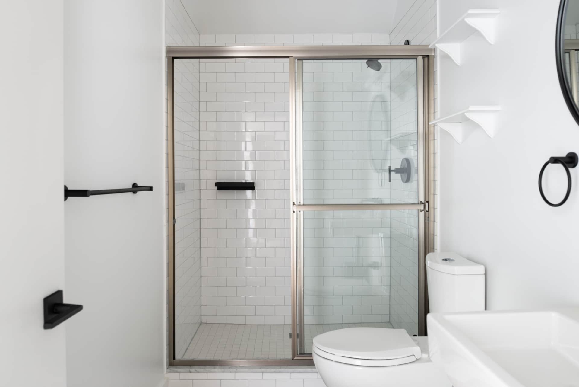 Modern bathroom with walk-in shower featuring white subway tiles, black accents, and a glass door, along with a white toilet and sink.