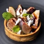 Mini fruit tart topped with whipped cream, chocolate chunks, and fresh mint leaves on a black background.