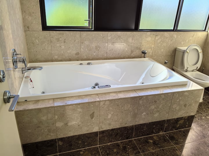 A modern bathroom with a large built-in bathtub and a toilet, tiled walls, and frosted windows.