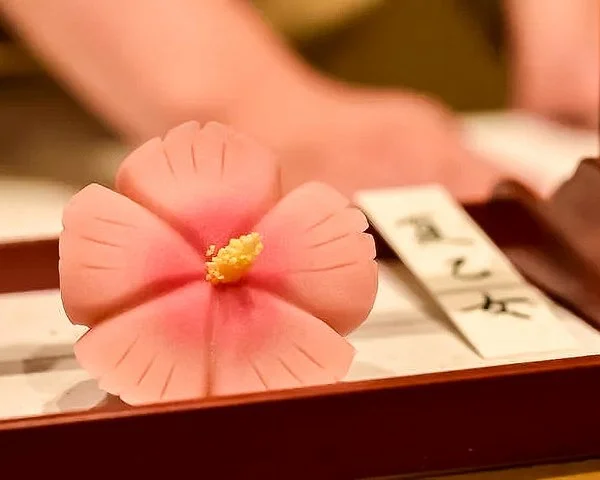 A pink hibiscus flower with yellow stamen placed on a table with Japanese writing paper.