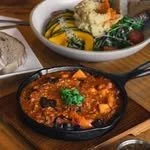 A bowl of chili topped with shredded cheese and green herbs, with a spoon nearby.
