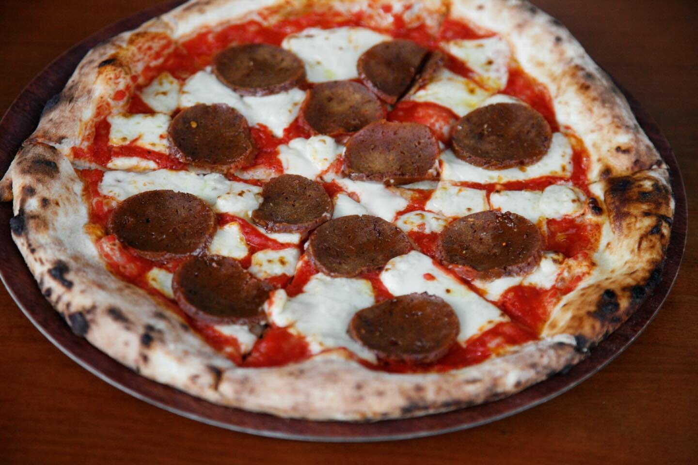 A pizza with pepperoni and mozzarella cheese on a wooden table.