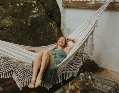 A woman relaxing and smiling on a hammock in an outdoor setting.