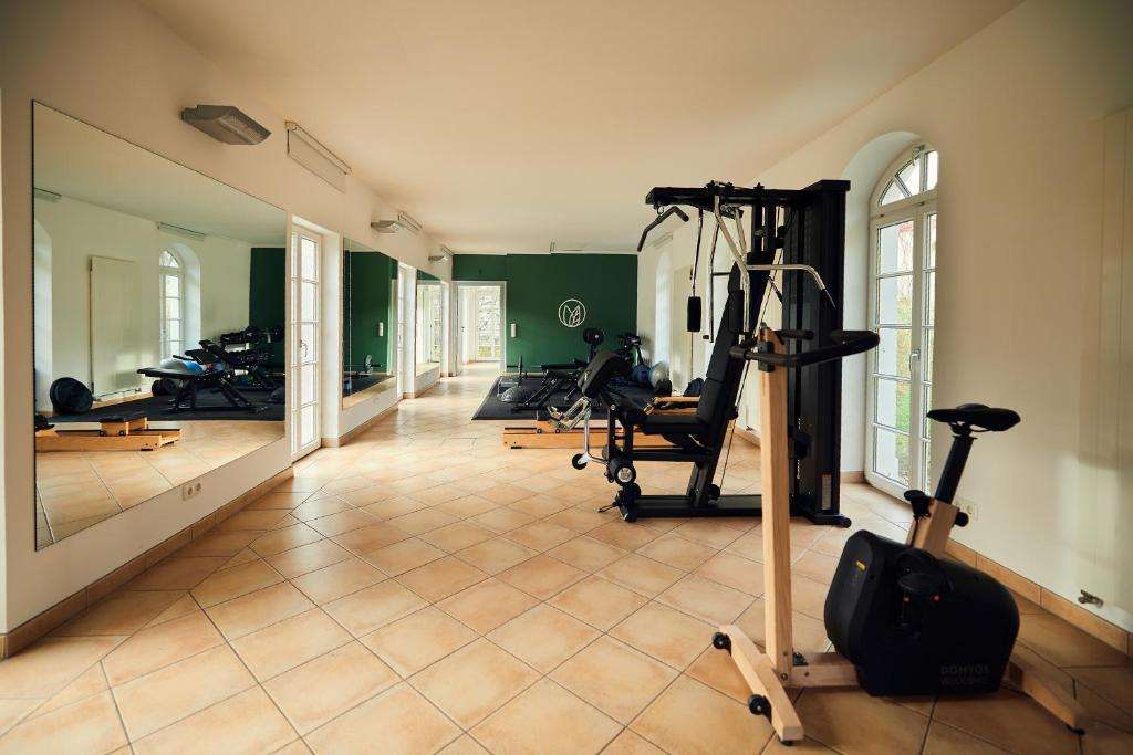 Empty gym room with exercise equipment, large mirror on wall, and windows letting in natural light.
