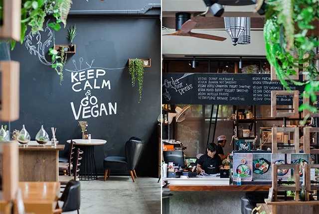 Interior of a vegan cafe with black walls, hanging greenery, and a chalkboard menu.