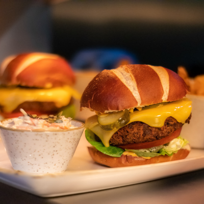 Cheeseburger with mustard, lettuce, pickles, and a beef patty, served with a side of coleslaw.